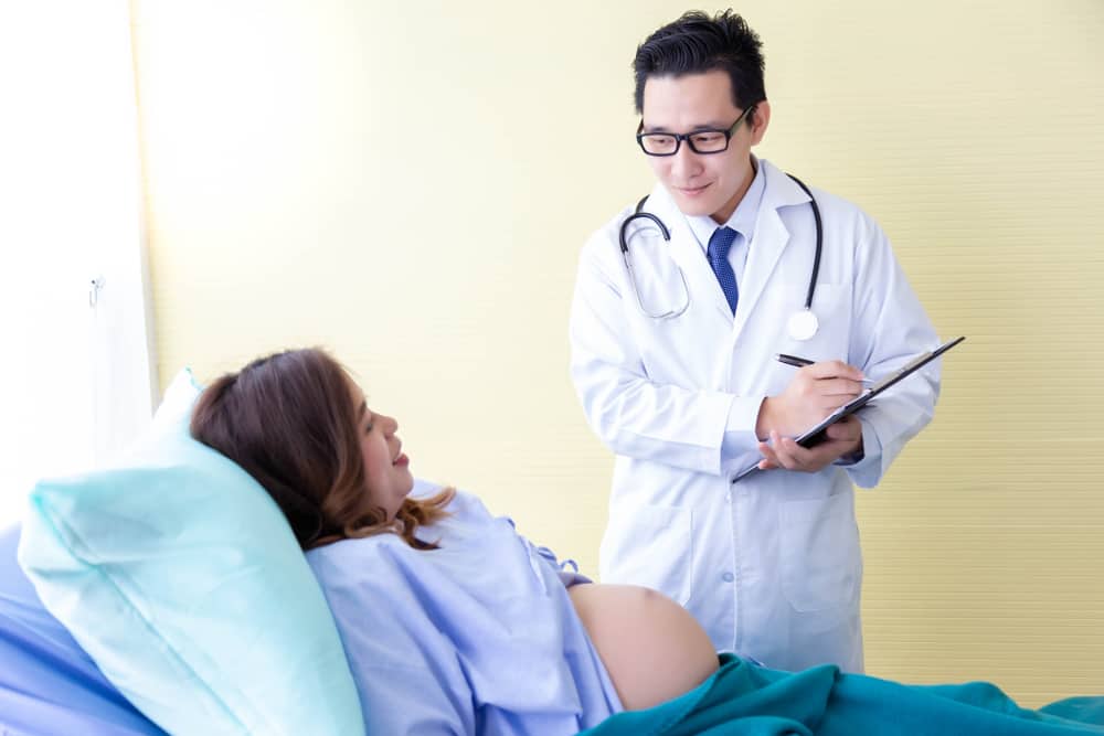 Handsome young doctor tell results of her health and her fetus that beautiful mom or mother, her child have good health. Doctor is checking and writing paperwork and look after his patient in hospital