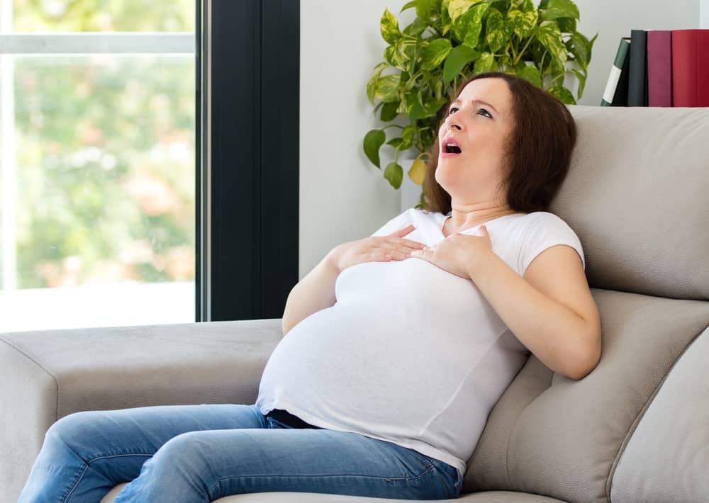 Pregnant woman suffering an anxiety attack alone at home; preeclampsia shortness of breath concept