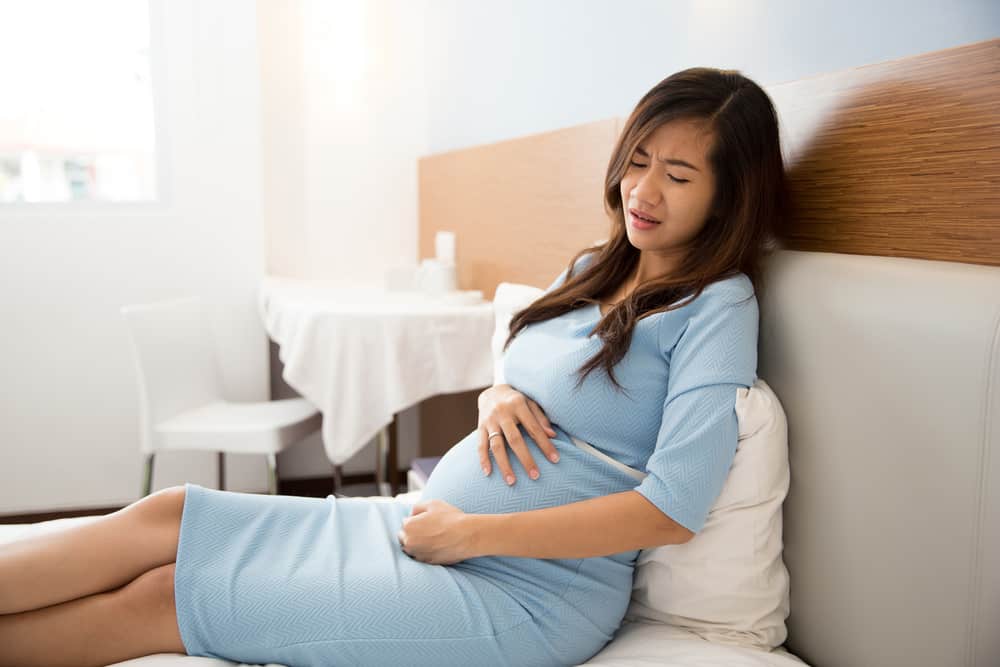 A portrait of an Asian pregnant woman has stomachache sitting on her bed