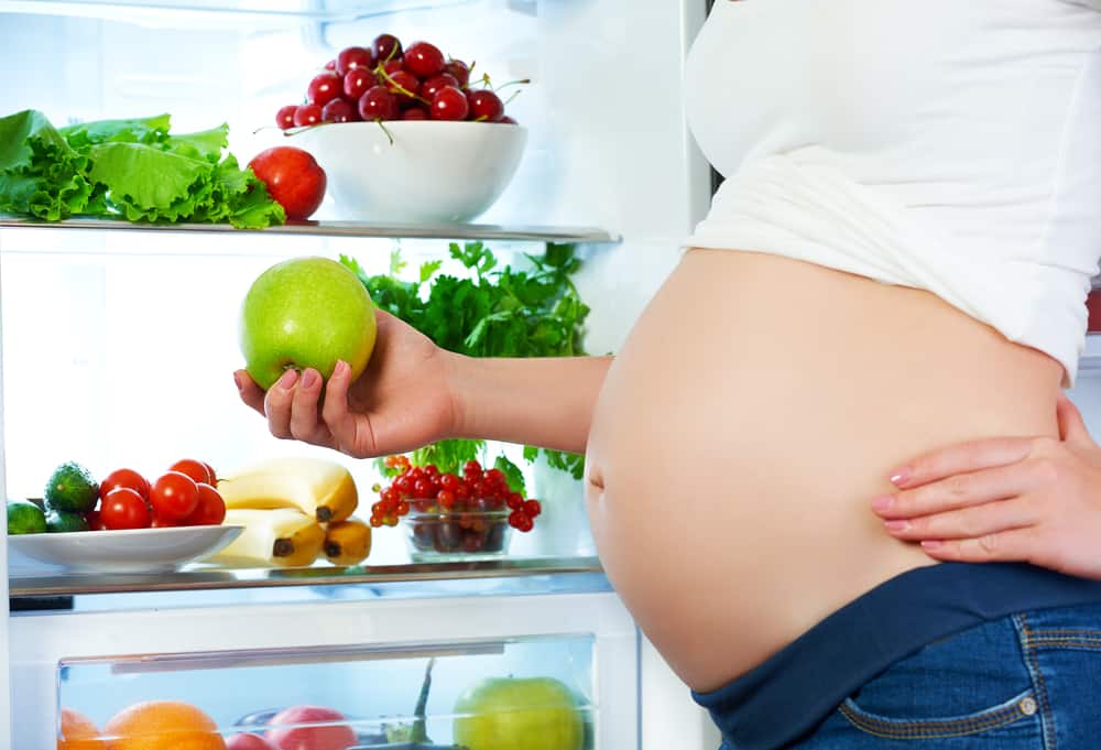 nutrition and diet during pregnancy. Pregnant white woman standing near refrigerator with fruits and vegetables