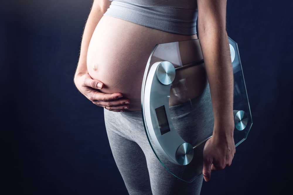 Pregnant woman holding scales and weigh keeping one hand on a belly. The concept of weight loss and control during pregnancy